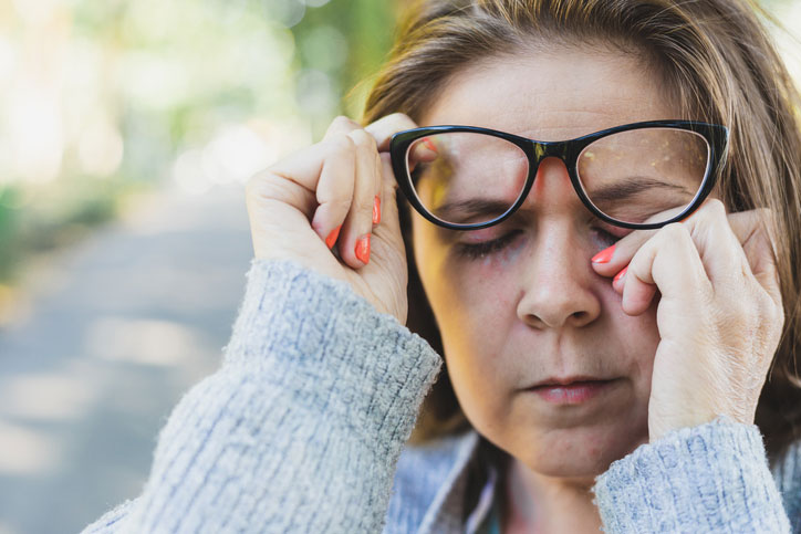 Woman with glasses rubbing her eyes due to dry eye symptoms.
