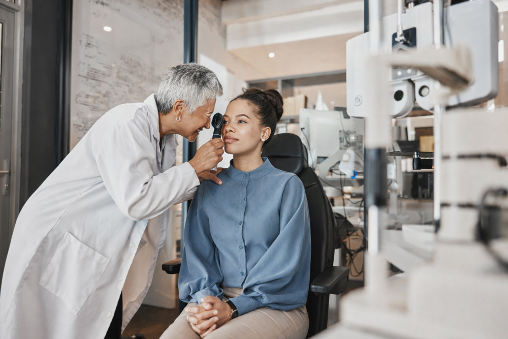 Ophthalmologist performing a detailed PRK pre-operative eye exam using a handheld ophthalmoscope on a young female patient seated in a modern eye care clinic.
